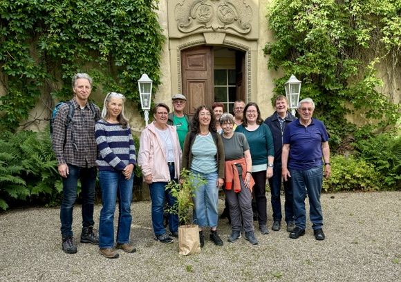 Eine Gruppe von Menschen steht vor einer Reben-umrangten Tür eines alten Schlosses. Sie lächeln freundlich in die Kamera.